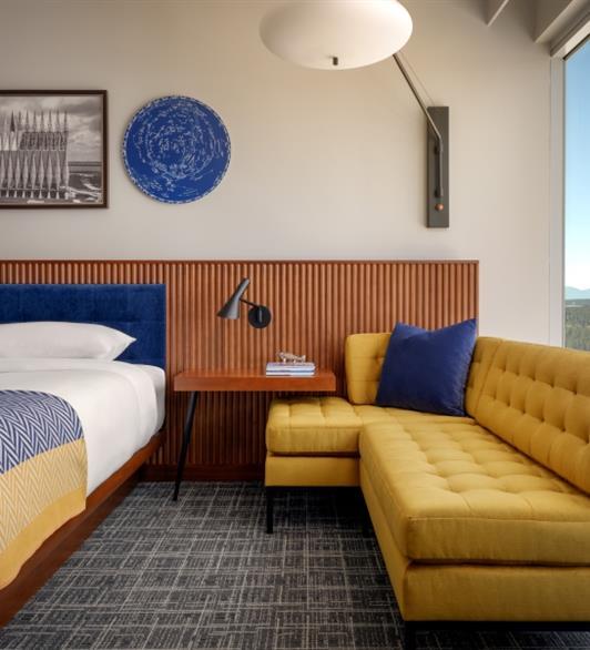 A yellow sofa next to a bed, with a desk in between the two