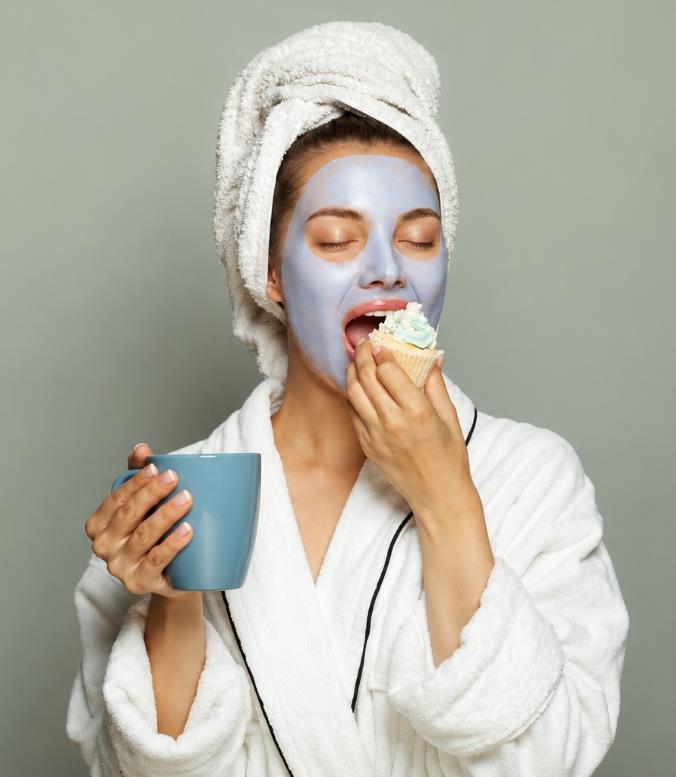 A lady eating a cupcake and drinking tea or coffee 