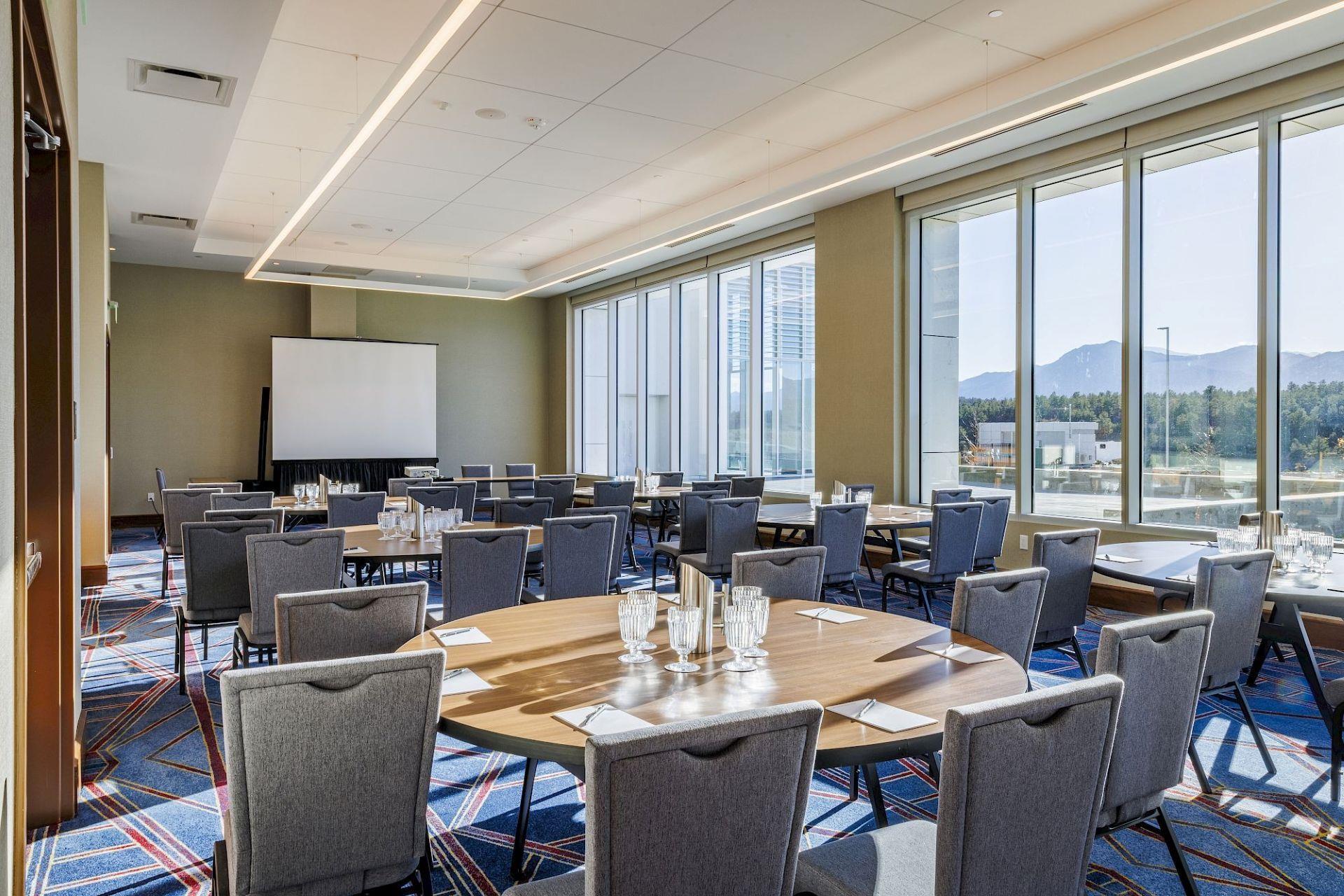 Meeting room at Hotel Polaris set for a conference with round tables, presentation screen, floor-to-ceiling windows, and scenic views of the Rocky Mountains.