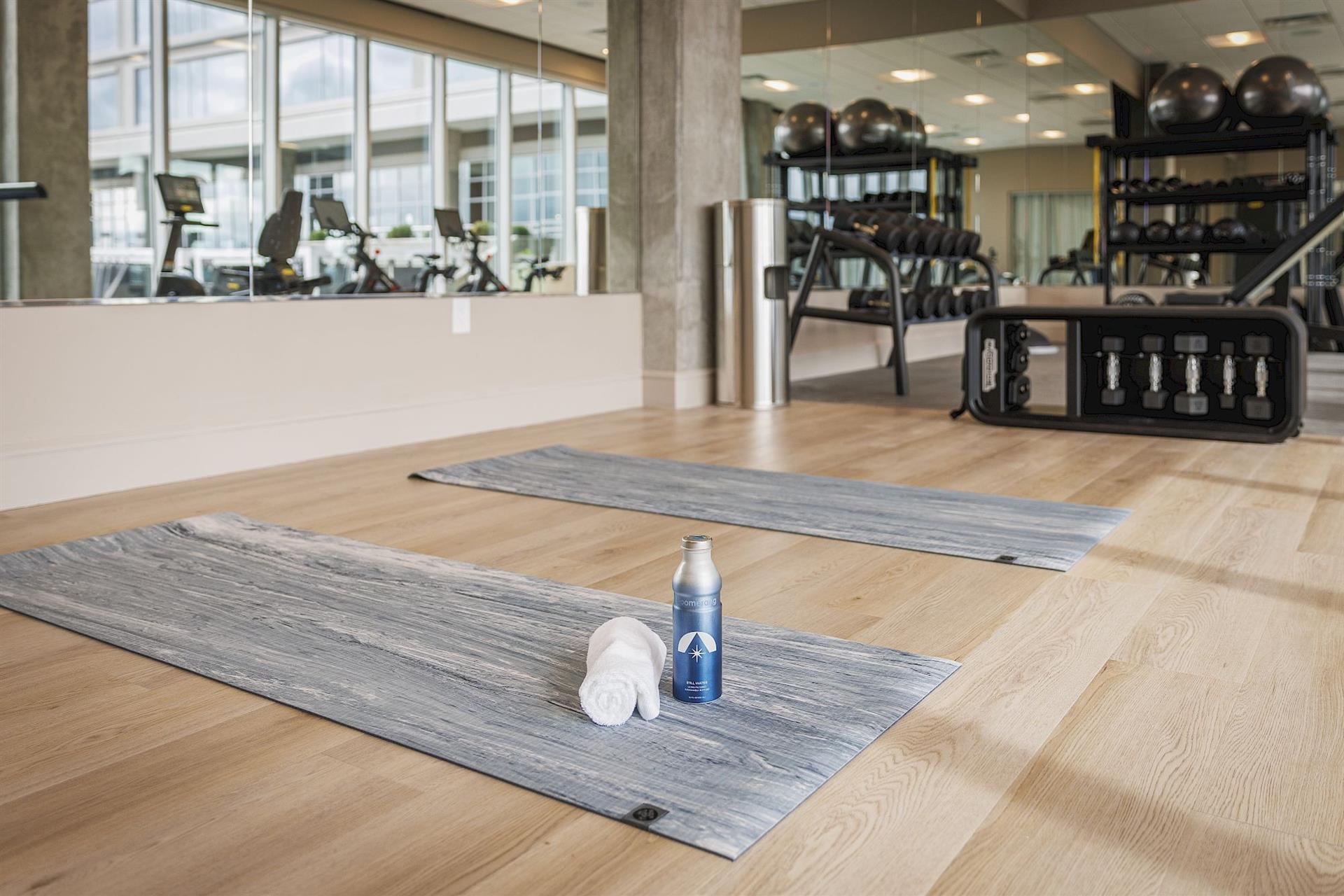 Fitness center at Hotel Polaris featuring a dedicated stretching area with yoga mats, free weights, cardio equipment, and floor-to-ceiling mirrors in a bright, modern workout space.