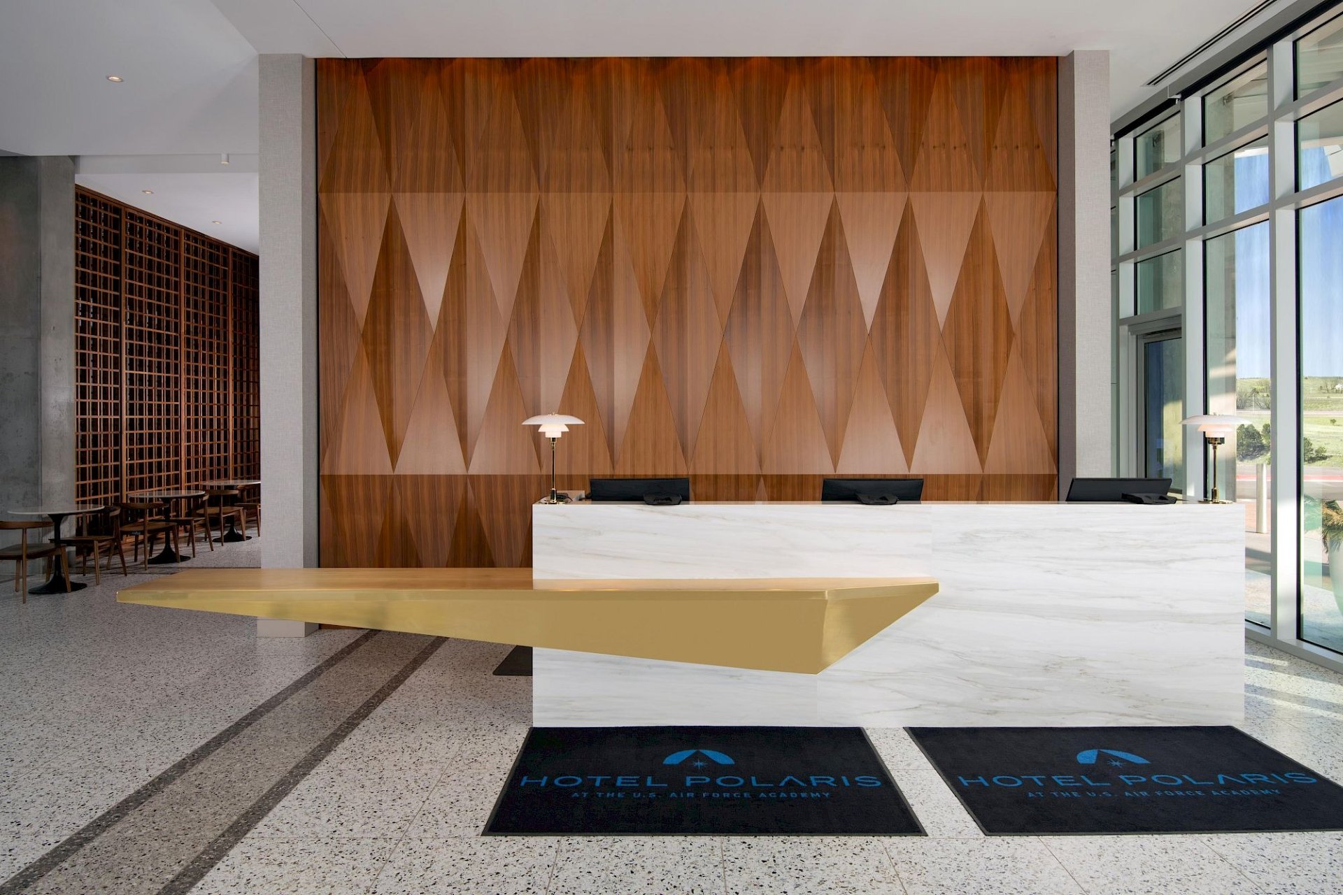 Hotel Polaris front desk featuring a white marble reception counter, geometric wood wall, and floor-to-ceiling windows.
