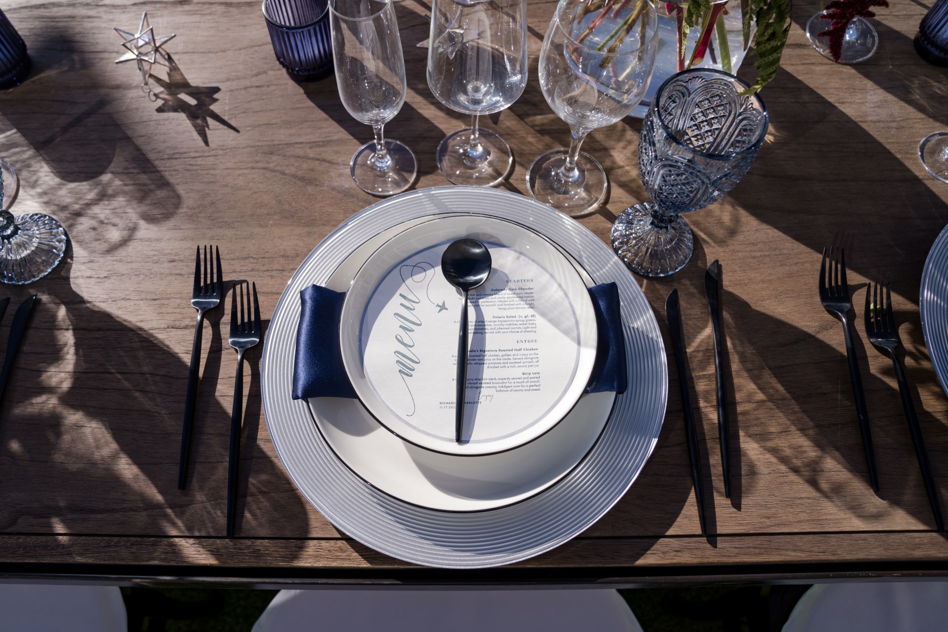 Elegant wedding place setting at Hotel Polaris featuring white dinnerware, navy napkin, black flatware, crystal glassware, and a printed menu on a wooden table.