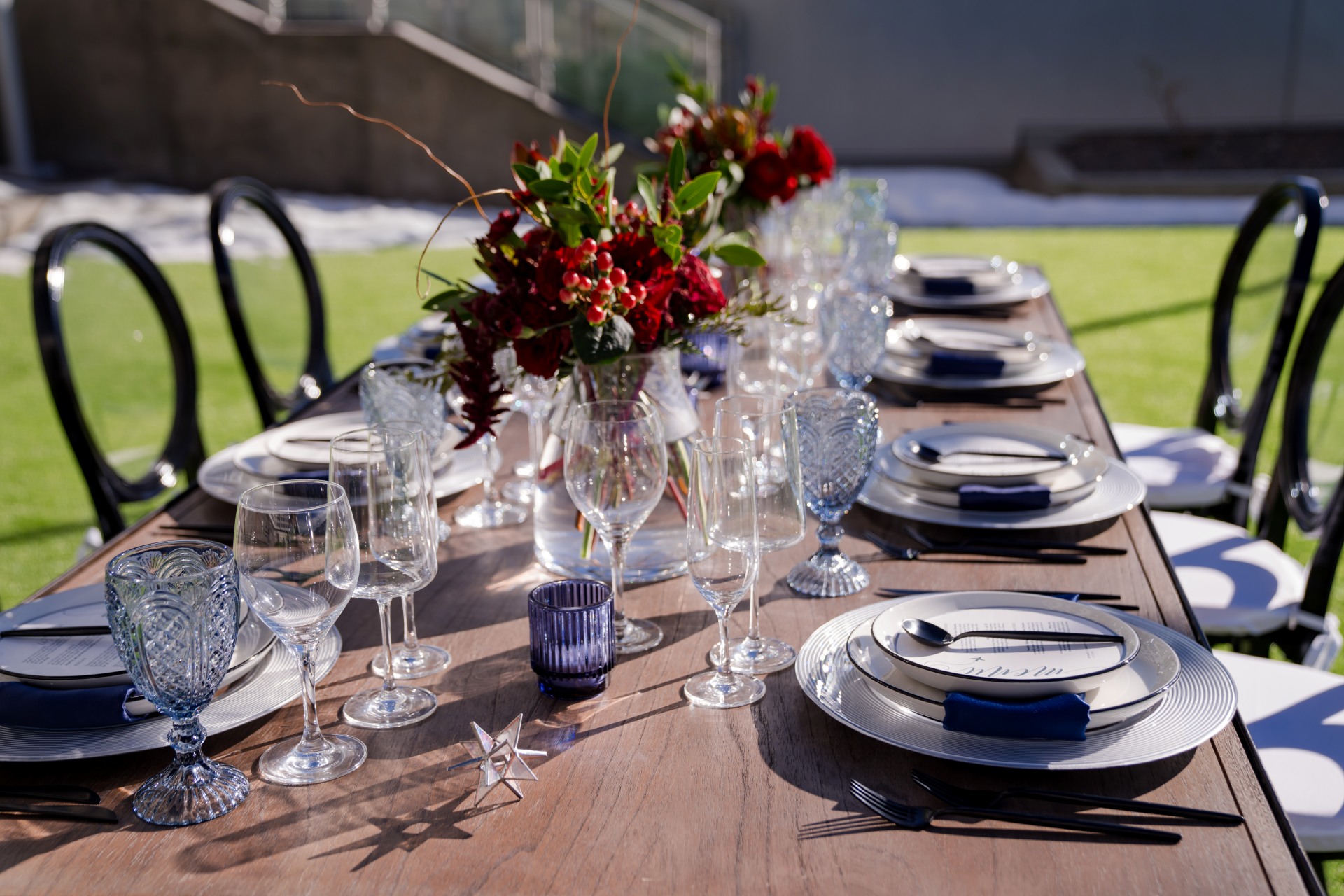 Outdoor wedding reception table at Hotel Polaris set with elegant dinnerware, crystal glassware, navy accents, and deep red floral centerpieces.