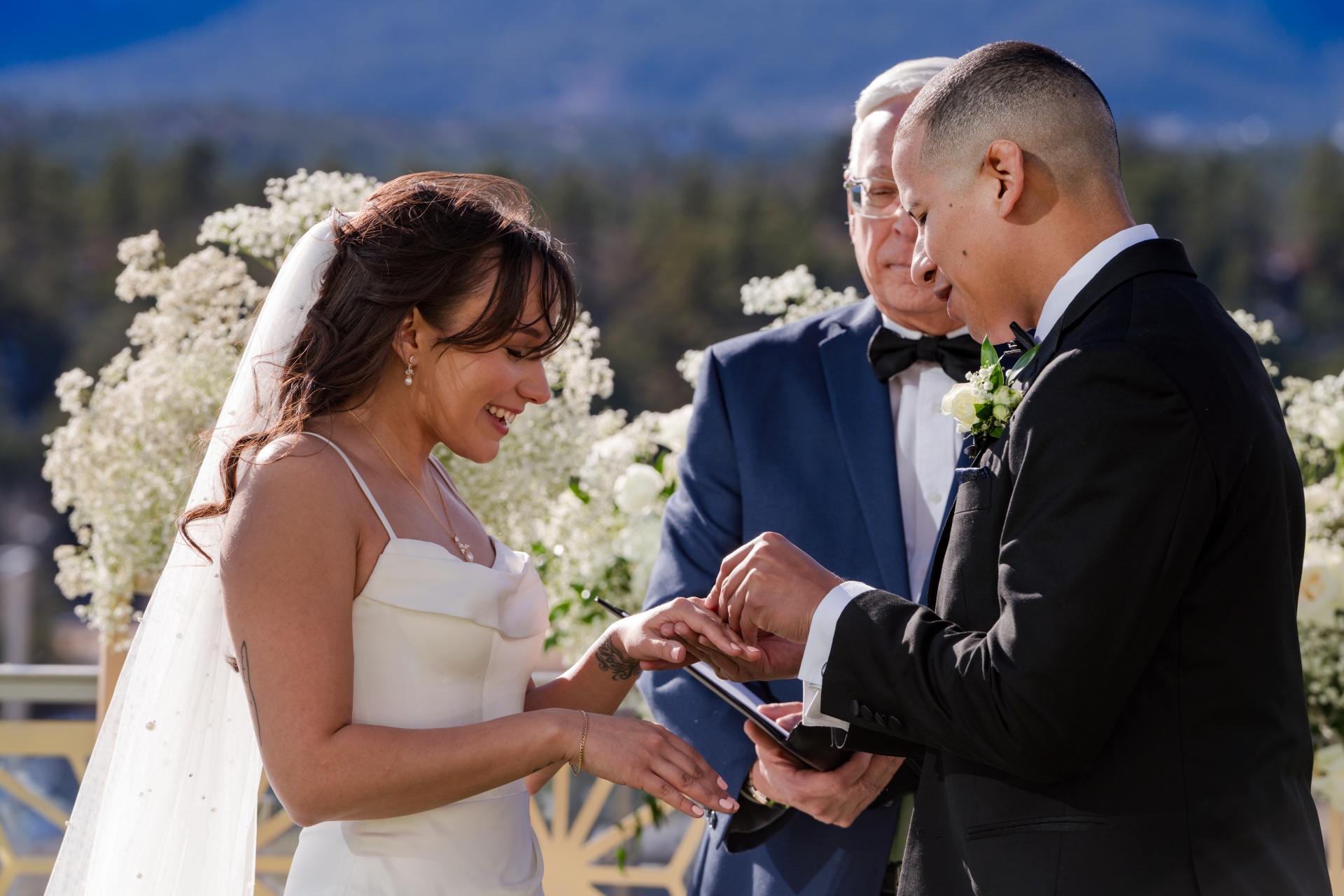 Bride and groom exchange rings during an outdoor wedding ceremony at Hotel Polaris, with mountain views and white floral arrangements.