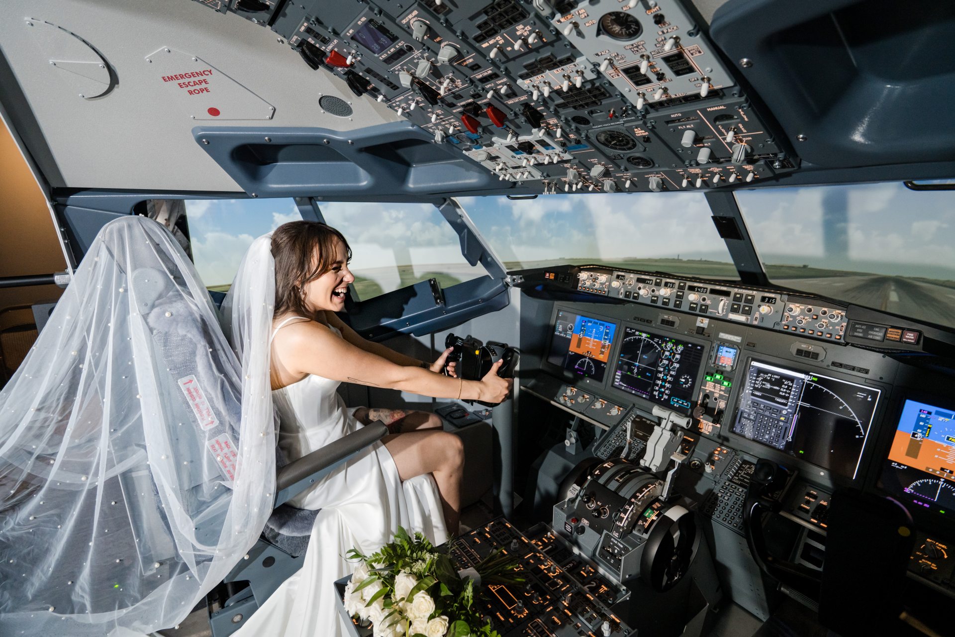 Bride seated in the cockpit of Hotel Polaris' commercial flight simulator, smiling as she operates the controls while wearing a wedding dress and veil.