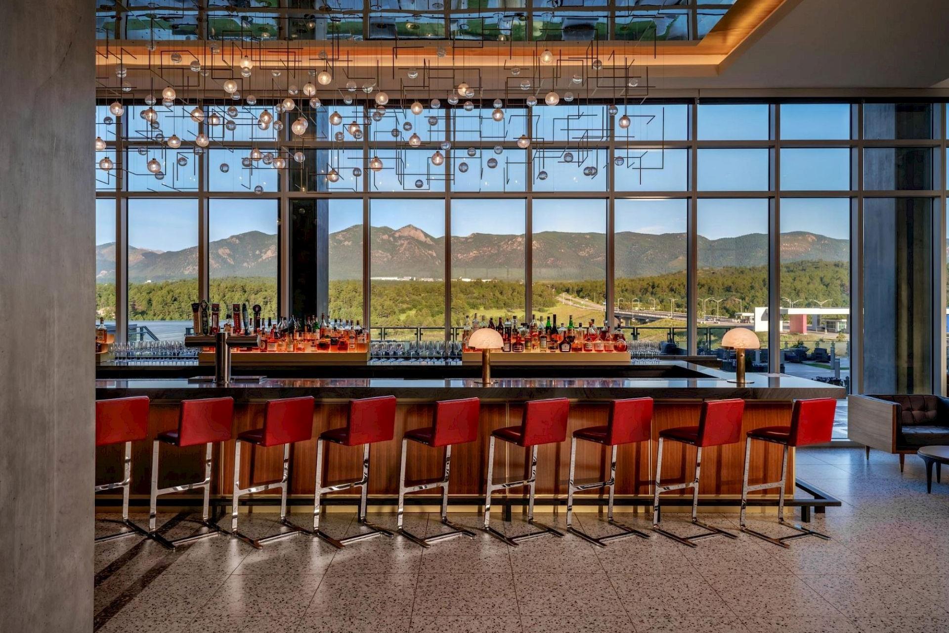 Hotel Polaris lobby bar featuring modern red bar stools, contemporary lighting, floor-to-ceiling windows, and panoramic views of the Rocky Mountains.