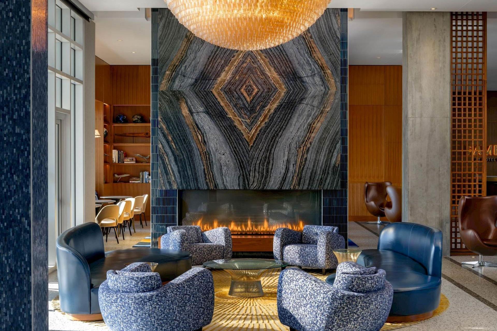Hotel Polaris lobby lounge featuring blue chairs around a fireplace beneath a statement chandelier and stone feature wall.