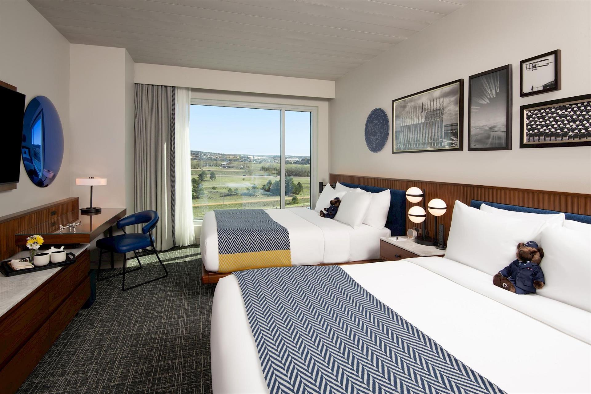 Double queen guest room at Hotel Polaris featuring modern aviation-inspired décor, plush bedding, a workspace, in-room coffee station, and large windows with views of the surrounding Colorado landscape.