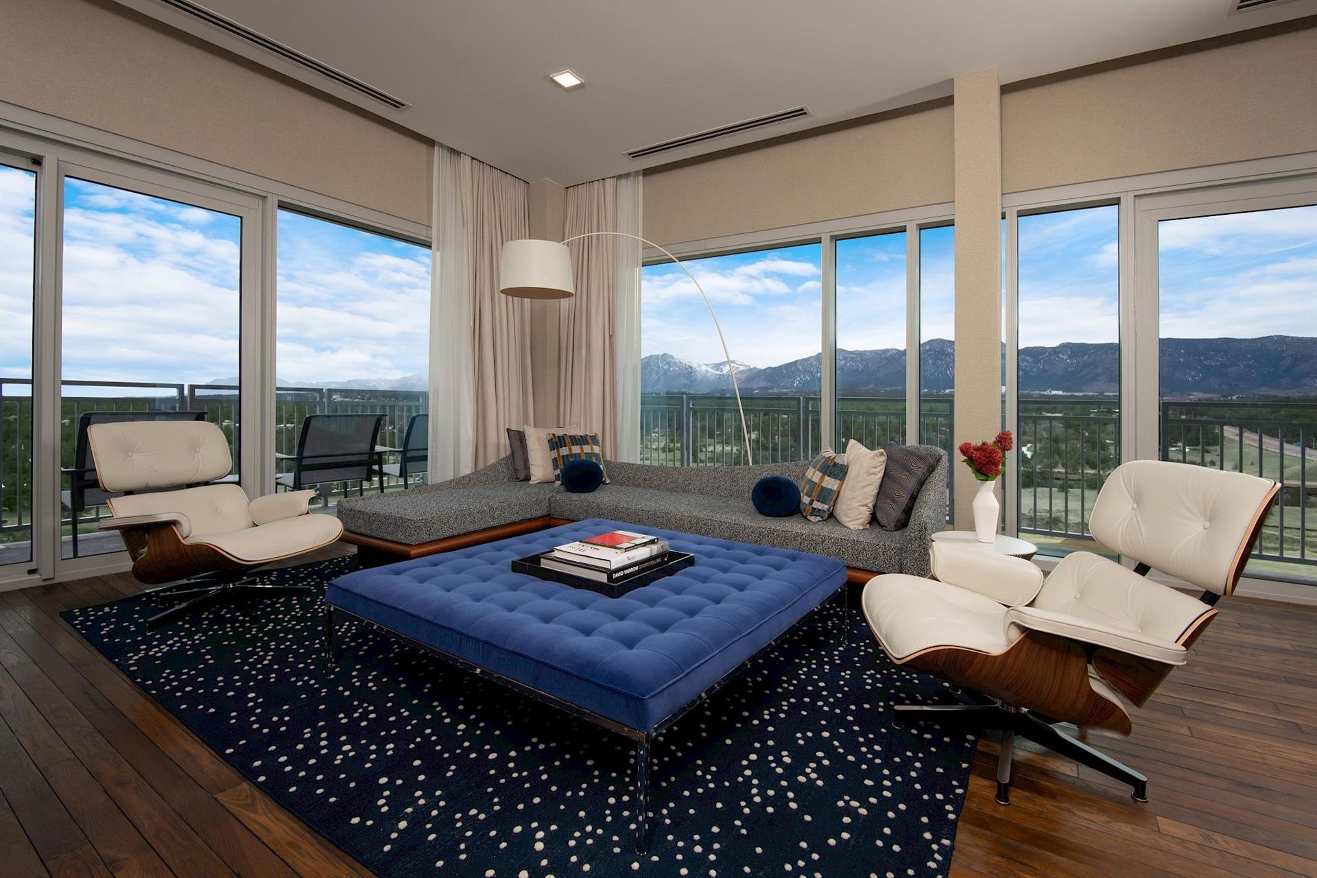 Luxury suite living room at Hotel Polaris featuring contemporary furnishings, floor-to-ceiling windows, a private balcony, and sweeping views of the Rocky Mountains.