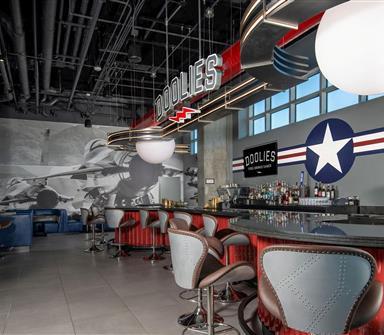 Aviation-themed sports bar with red bar counters, aircraft-inspired seating, large jet mural, military-style star graphic, and Doolies signage.