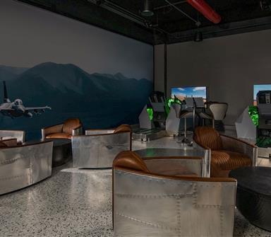 Aviation-themed lounge at Hotel Polaris featuring leather club chairs, aircraft-inspired furnishings, and immersive fighter jet flight simulators for guests to enjoy.