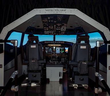Commercial flight simulator at Hotel Polaris featuring a full-scale aircraft cockpit with dual pilot seats, illuminated flight controls, and an immersive runway simulation experience.