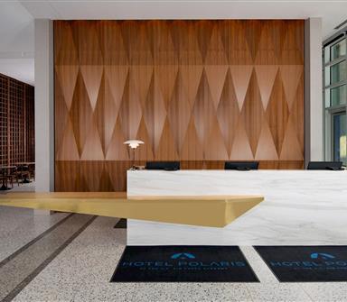 Hotel Polaris front desk featuring a white marble reception counter, geometric wood wall, and floor-to-ceiling windows.