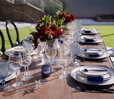Outdoor wedding reception table at Hotel Polaris set with elegant dinnerware, crystal glassware, navy accents, and deep red floral centerpieces.