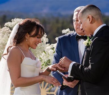 Bride and groom exchange rings during an outdoor wedding ceremony at Hotel Polaris, with mountain views and white floral arrangements.