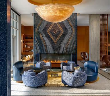 Hotel Polaris lobby lounge featuring blue chairs around a fireplace beneath a statement chandelier and stone feature wall.