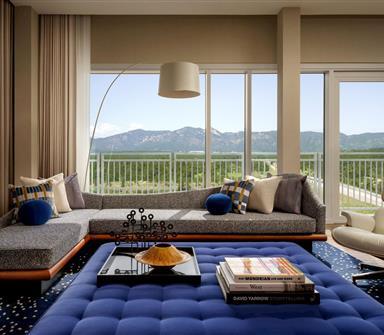 Luxury suite at Hotel Polaris featuring a contemporary lounge with designer furnishings, floor-to-ceiling windows, a private balcony, and panoramic views of the Rocky Mountains.