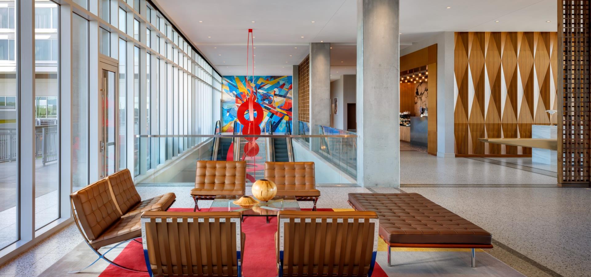 A modern hotel lobby with a seating area, large artwork, and a glass wall