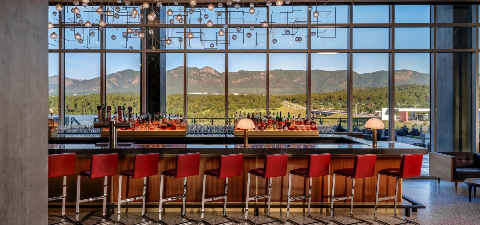 A bar with red stools and a large window showing a mountain view.