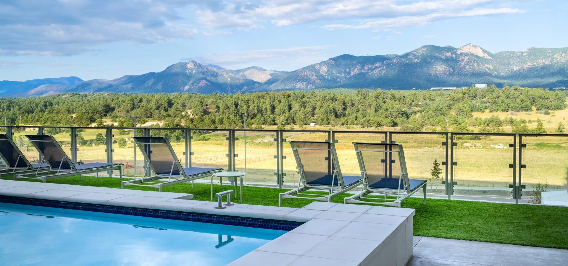 A pool area with lounge chairs, a grassy area, and a mountain view.