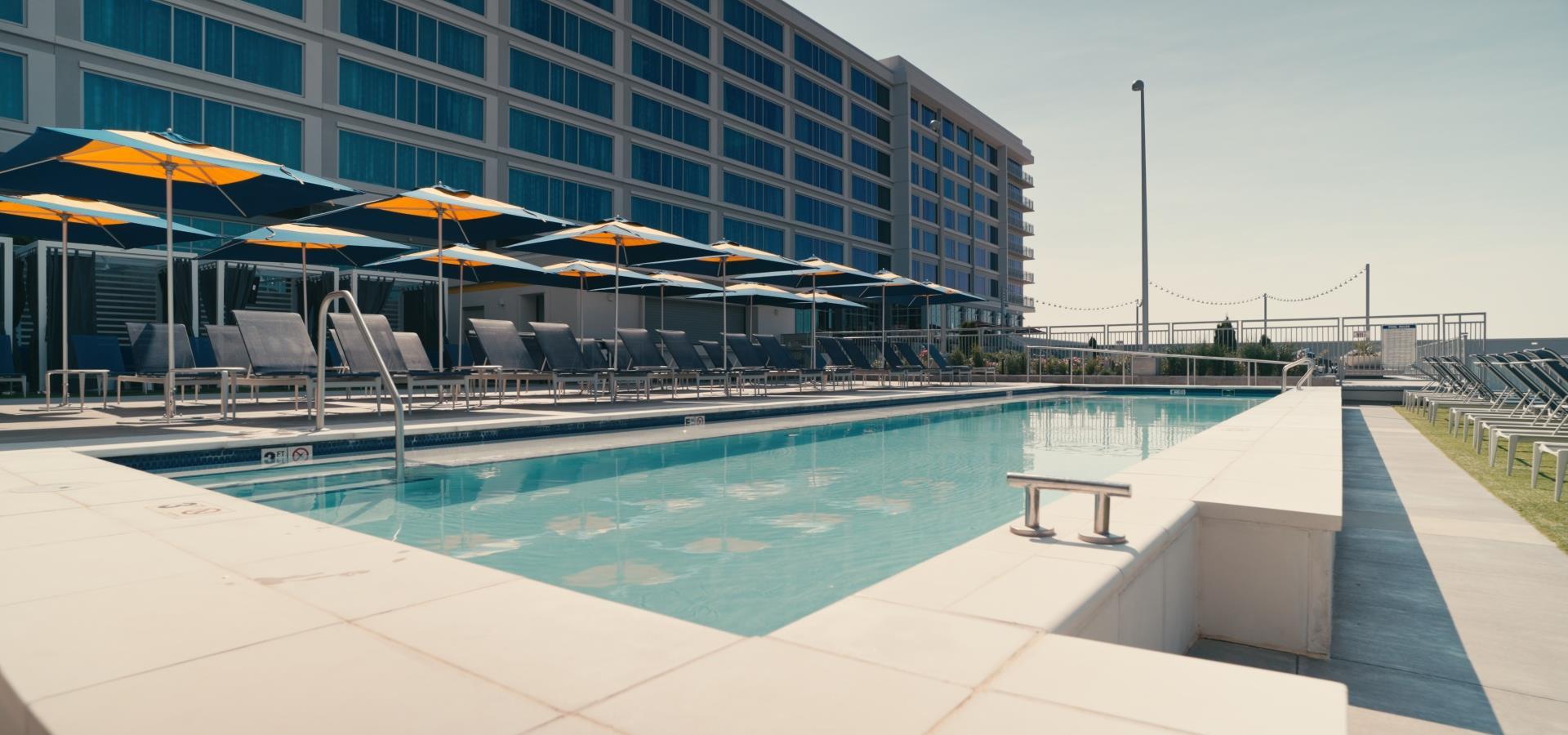 A pool with lounge chairs and umbrellas in front of a large building
